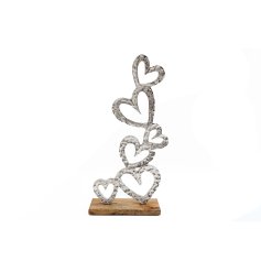 Numerous silver heart decorations with cut out details on a wooden base. 