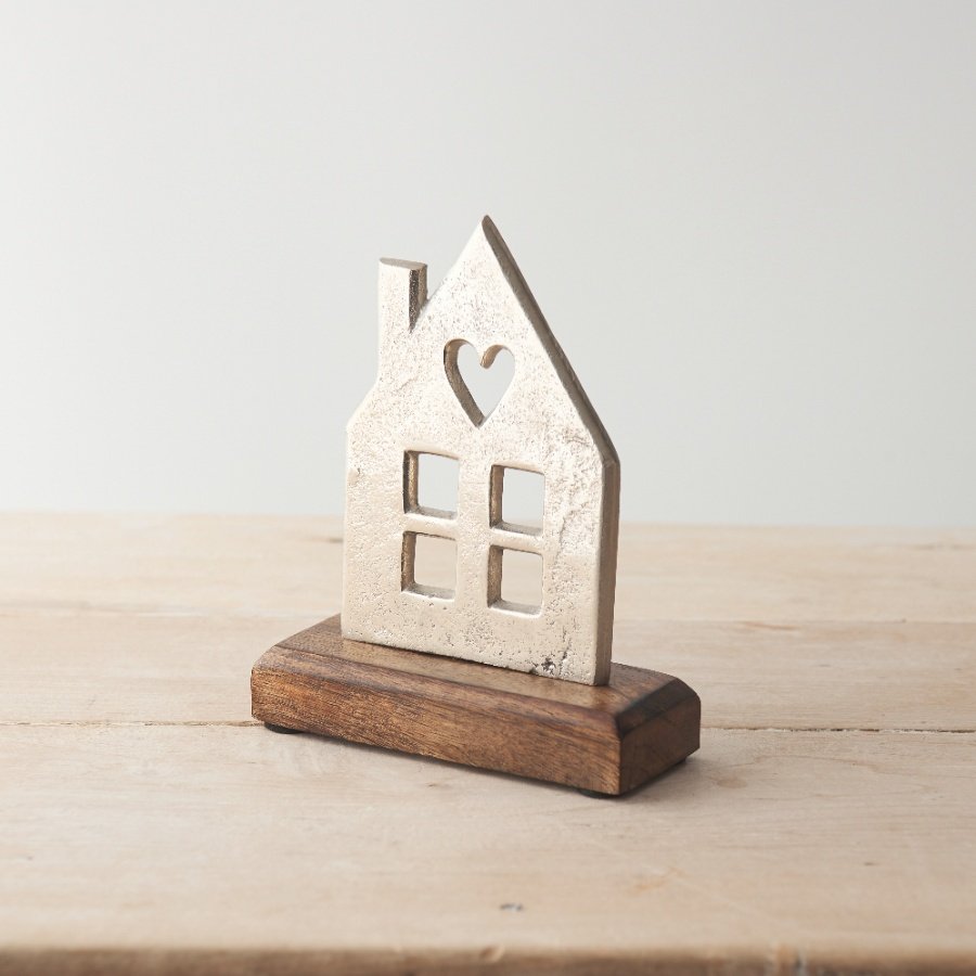 A stylish decoration featuring a metallic silver house with cut out details and heart motif, presented on a wood base. 