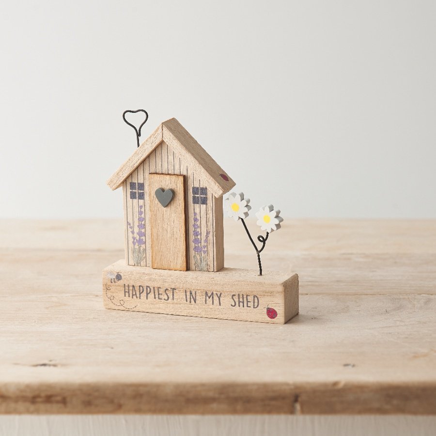 A wooden decoration with shed design alongside "happiest in my shed" text with wire detailing and floral touches. 