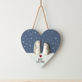 a rustic heart shape sign hung from jute string featuring two penguins in the snow