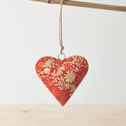 A colourful metal hanging heart decoration with a rich orange hue and white botanical design. 