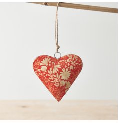 A colourful metal hanging heart decoration with a rich orange hue and white botanical design. 