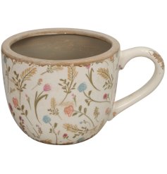 A distressed planter in a mug shape detailing an illustrated array of flowers.