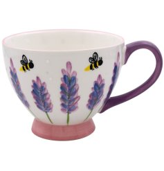 A charming footed mug with a lavender and bee design. It details a wide spout and chunky purple handle.