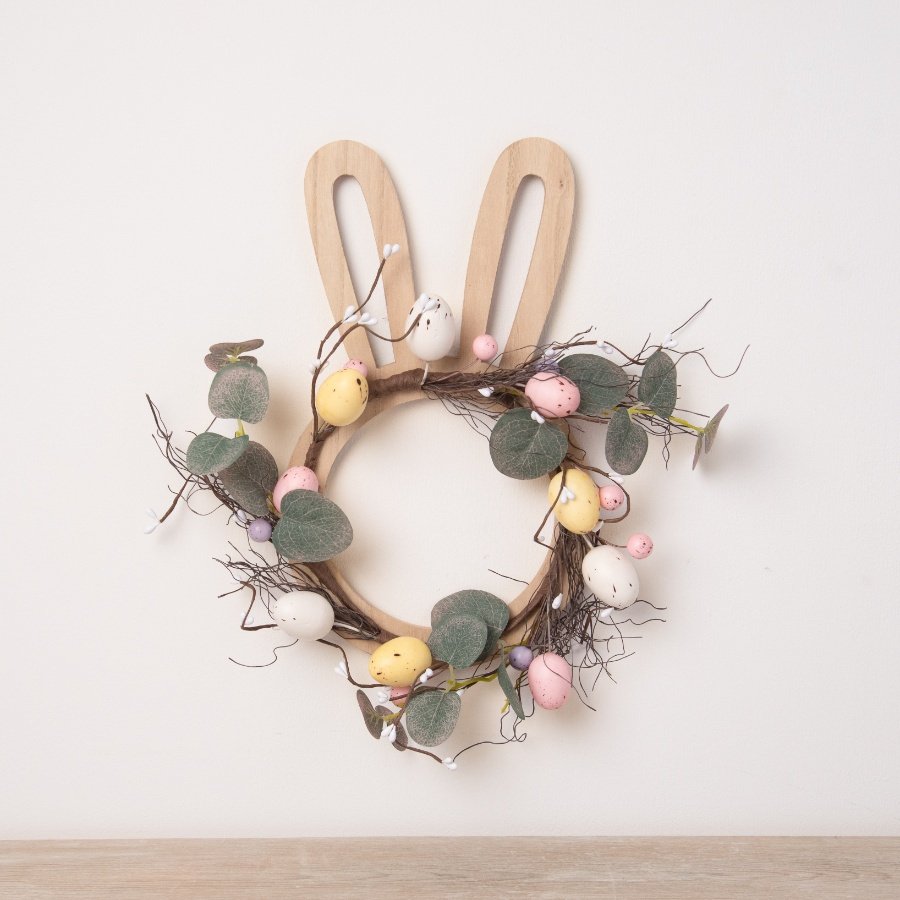 A contemporary Easter wreath featuring a wooden bunny frame adorned with a rustic twig wreath. 