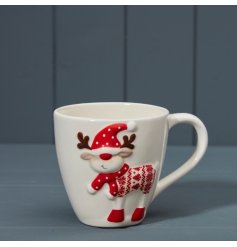 A Christmas mug in white with an embossed reindeer design, wearing a Christmas jumper and red polkadot scarf.