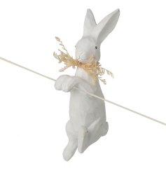 A white etched rabbit pot hanger holding a sprig of natural foliage. 