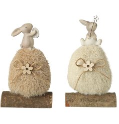 2 assorted bunny ornaments featuring a large wool egg resting on a log base, with a cute bunny sat ontop