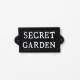 A dainty black sign with ' Secret Garden' text in white. 