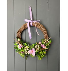 A gorgeous wreath made from bound twigs, adorned with beautiful flowers and hand finished with a purple wreath for hangi