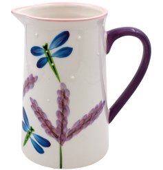 A glazed white jug featuring a purple handle dragonfly and flower paintings. 