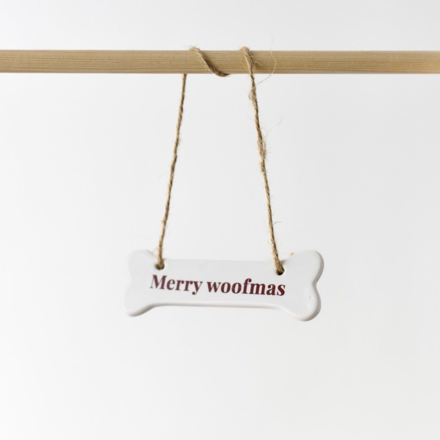 A delightful ceramic bone ornament embellished with the quote "Merry woofmas" in a vibrant red font.