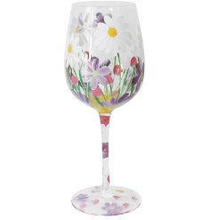 A chic wine glass featuring hand painted flowers and a greenery scene. 