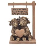 An adorable highland cow ornament featuring a pair of loving cows holding a heart sat under a sign.