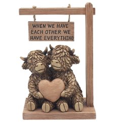 A charming highland cow ornament with a loving pair holding a heart, positioned beneath a sign
