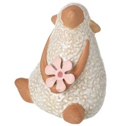 A cute sitting sheep ornament gazing into the sky whilst holding a springtime pink flower.