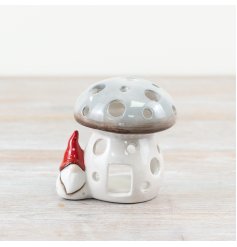 A grey ceramic mushroom candle house with cut-out circles complete with a little ceramic gonk with a red hat.