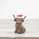 A delightful sitting highland cow with a Christmas hat made from resin