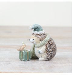A charming resin hedgehog adorned with a sage green hat and scarf, complete with a delightful present and a delicate lit