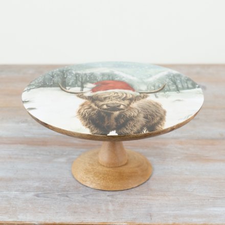 A mango wood cake stand with a festive highland cow design.