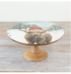 A mango wood cake stand with a festive highland cow design.