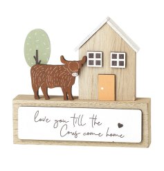 A charming wooden plaque featuring a highland cow set stood by a house decoration with scripted text.