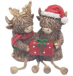 A charming Christmas ornament featuring two highland cows in Christmas accessories with a gift box. 