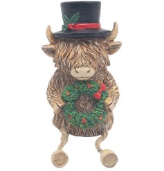 A Christmas highland cow shelf sitter with top hat and wreath. A unique seasonal decoration. 