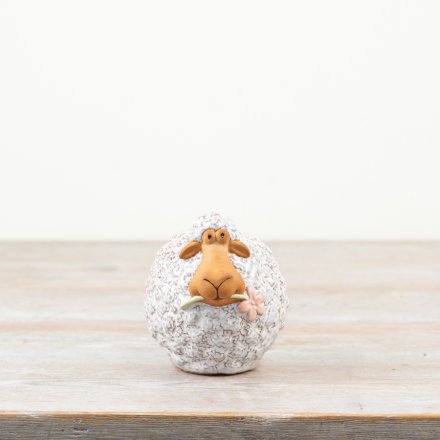 A wooly sheep stood holding a dainty pink flower in its mouth.