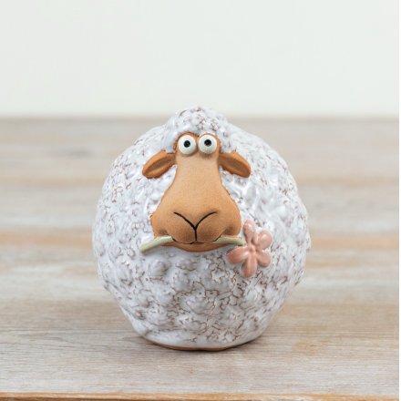 A wooly sheep stood holding a dainty pink flower in its mouth.
