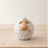 A wooly sheep stood holding a dainty pink flower in its mouth.