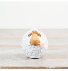 A wooly sheep stood holding a dainty pink flower in its mouth.