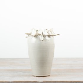 Delightful bird perched on rim of a natural-toned vase.