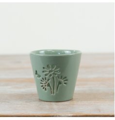 Discover this sage green glazed candle holder with a delicate flower cut-out silhouette.