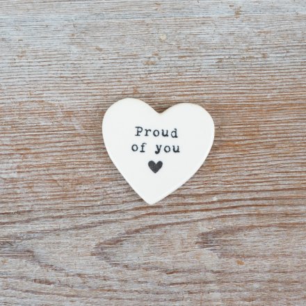 A delicate heart token embossed with "proud of you" in black, featuring a small heart below.