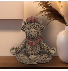 A charming rustic Highland cow ornament, part of the Hughie collection - sat in a yoga pose whilst wearing a tartan scar