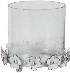 A glass candle holder set upon a rustic white metal base featuring small flowers. 