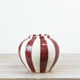 A decorative ceramic vase showcasing rich red vertical stripes layered over a subtly speckled cream background. 