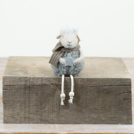 A soft fabric sitting sheep ornament featuring seasonal detailing and dangling legs