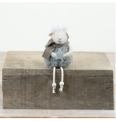 A soft fabric sitting sheep ornament featuring seasonal detailing and dangling legs