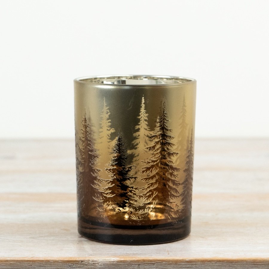 Glass tealight holder features a warm gold finish decorated with a delicate woodland tree pattern.