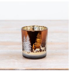 A decorative glass candle holder featuring a woodland scene with deer and trees