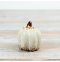 A pumpkin with a soft neutral glaze, featuring gently worn brown accents near the base and stem.