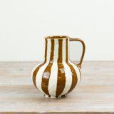 This ceramic jug-style vase combines a classic rounded form with a practical handle and a warm striped glaze